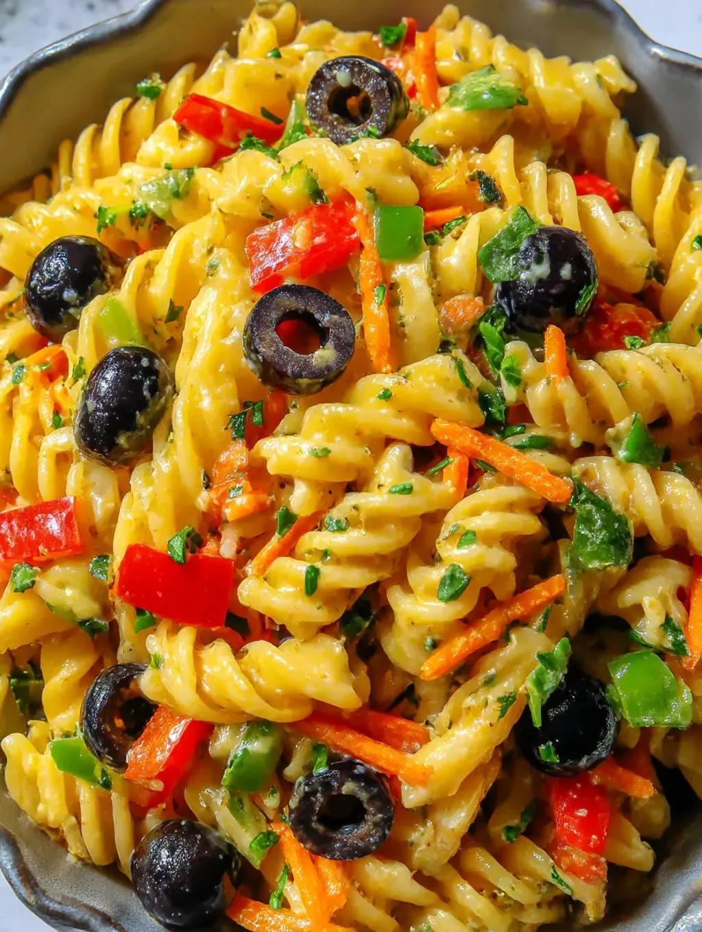 Ein Bild von einer Pasta Salat mit vielen Zutaten wie Karotten, Tomaten, Zwiebeln, Oliven und Basilikum.