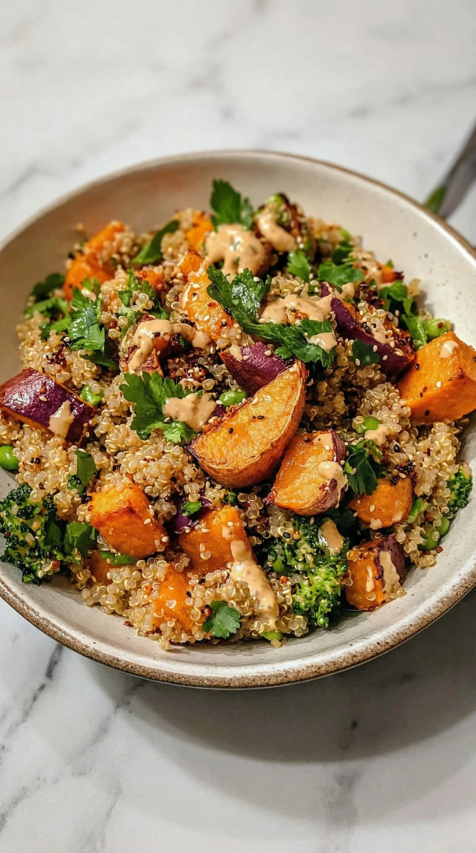 Ein Gerösteter Süßkartoffel-Quinoa-Salat mit Sesam-Miso-Sauce in einem glatten, silbernen Behälter.