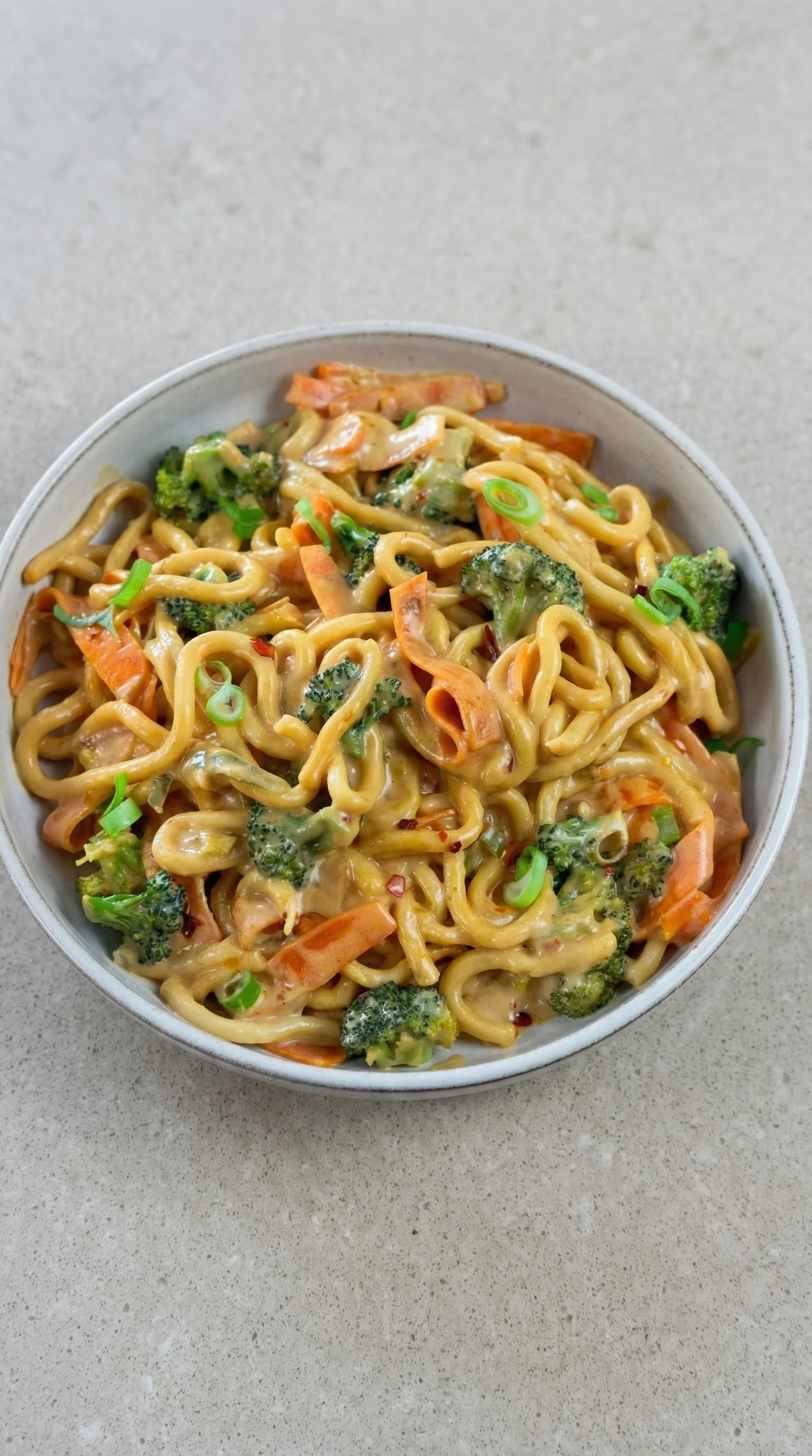 Ein Glas mit Udon Nudeln, die in einer Sauce mit Erdnuss und Gemüse getaucht sind.