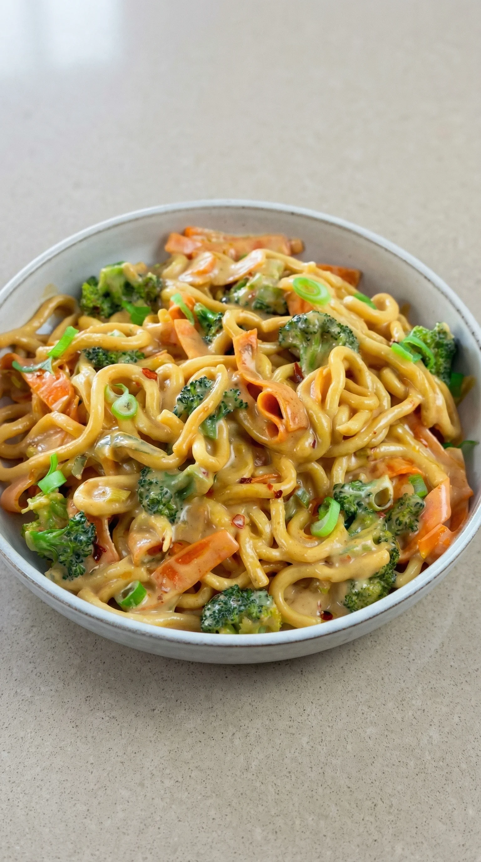 Ein Schälchen mit Udon Nudeln und Gemüse, darunter Brokkoli, Karotten und Zwiebeln.