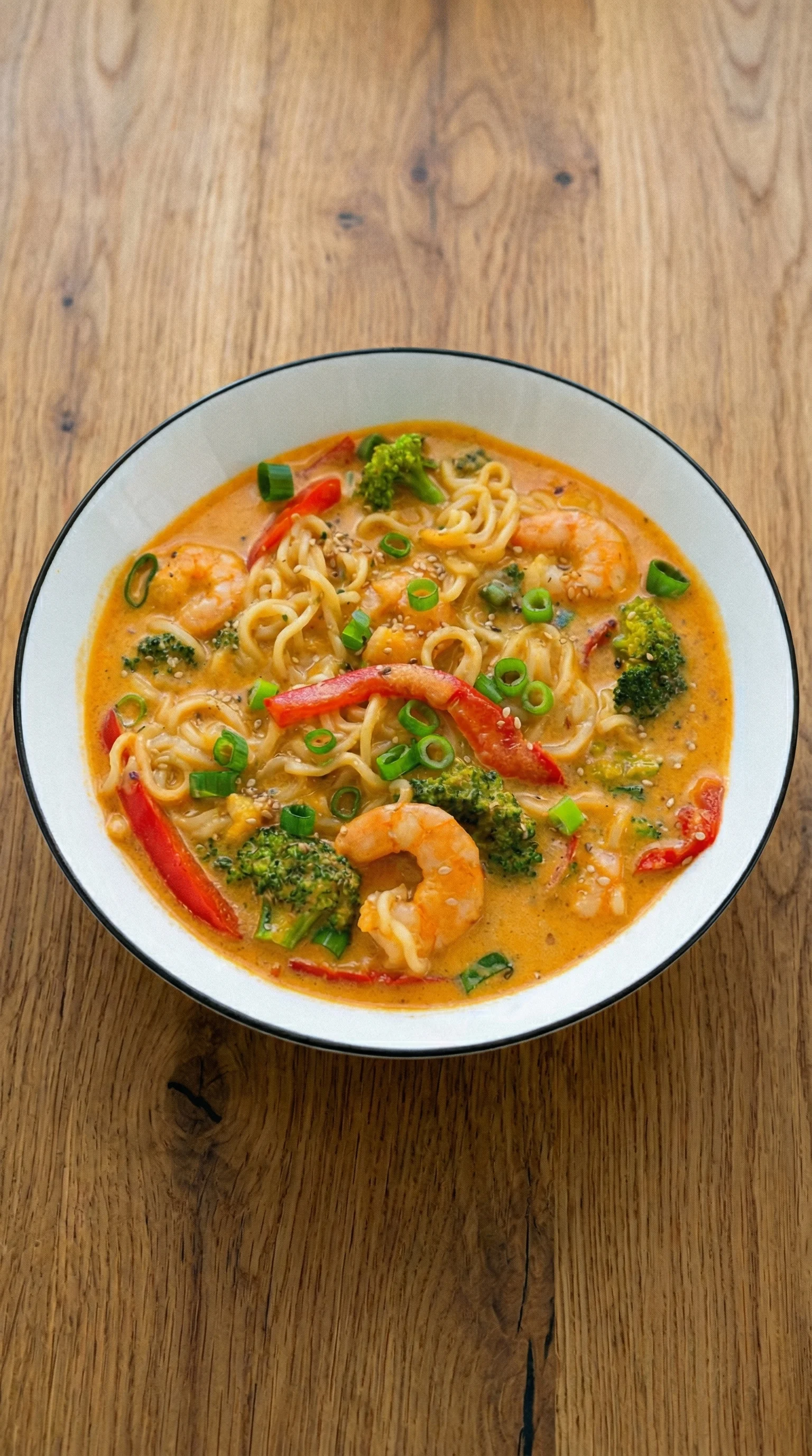 Ein weißer Teller mit einer asiatischen Nudelsuppe, die mit Garnelen und Zwiebeln garniert ist.