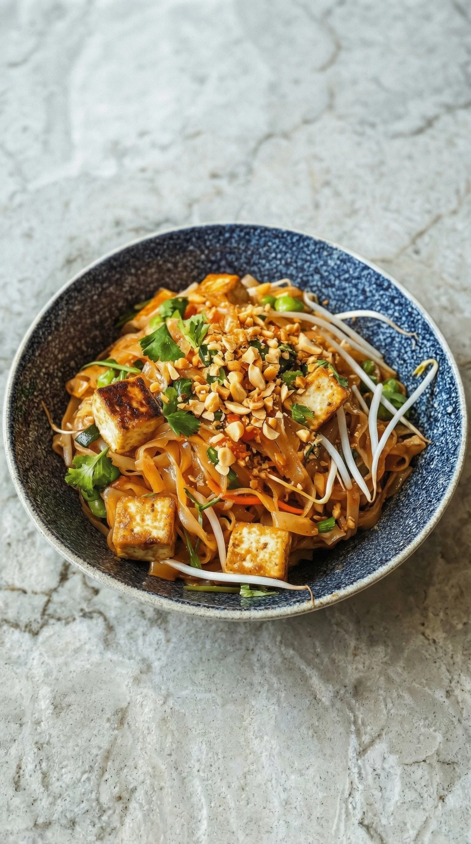 Ein Tofu Pad Thai in einem gl&auml;sernen Becher mit einer Kombination aus Tofu, Reis, Nudeln, Karotten, Sesam und Gew&uuml;rzen.