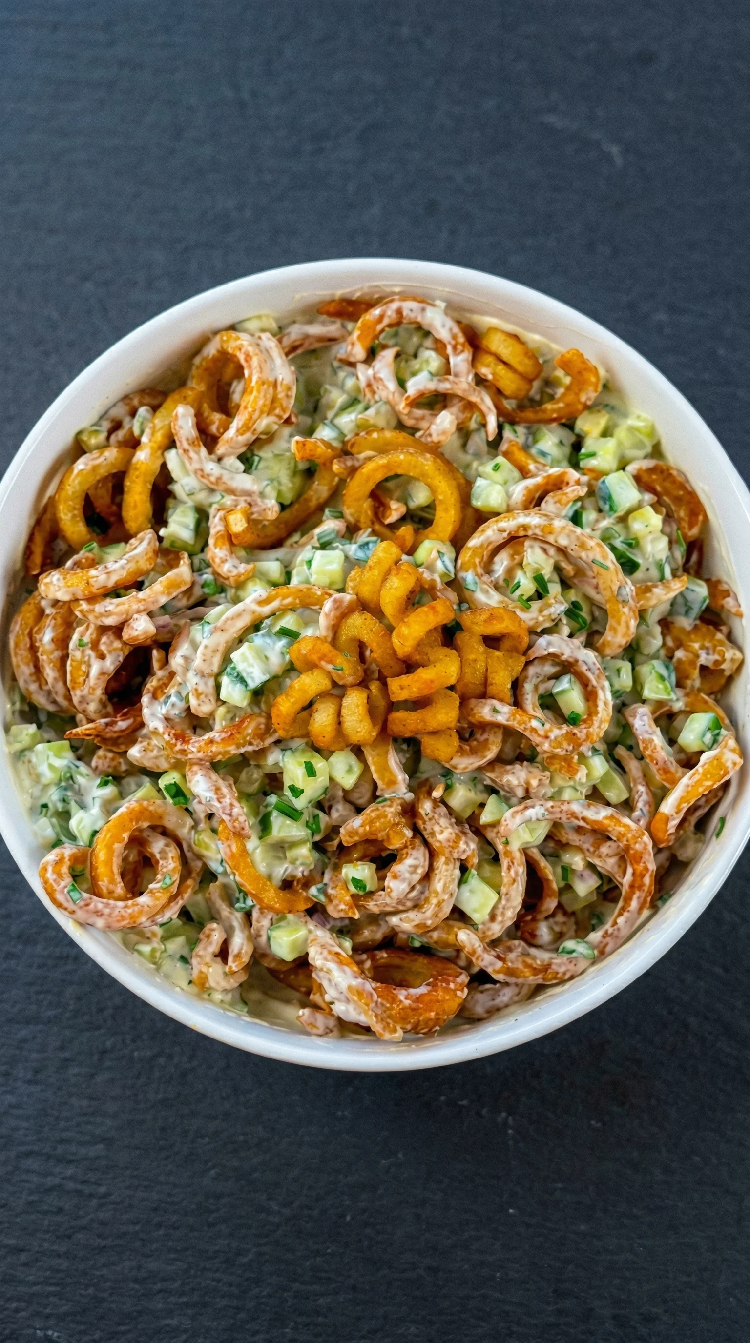 Ein großes, weißes Becher mit Curly Fries Salat und cremigem Dressing.