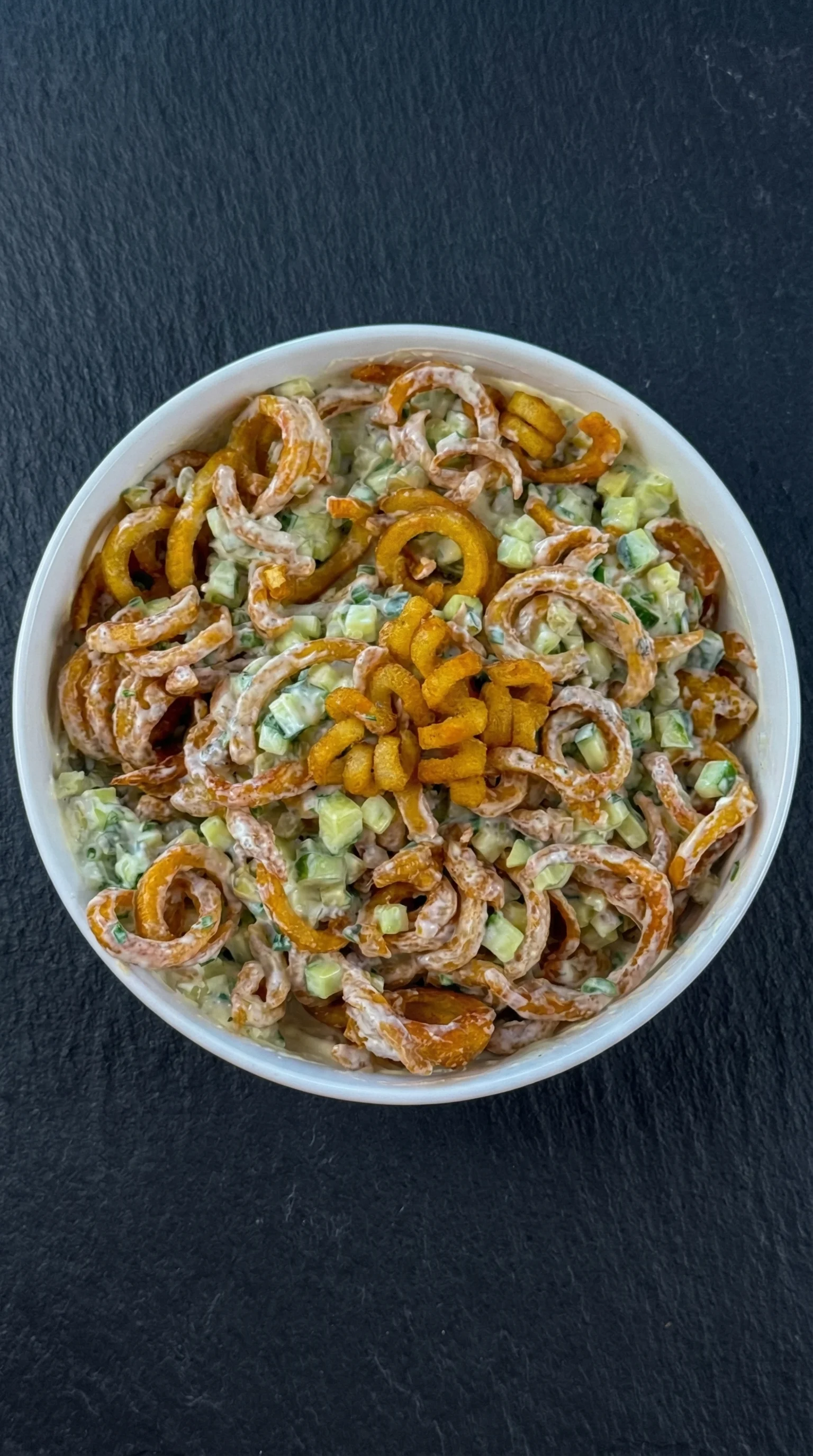 Ein weißer Becher mit Curly Fries Salat und cremigem Dressing.