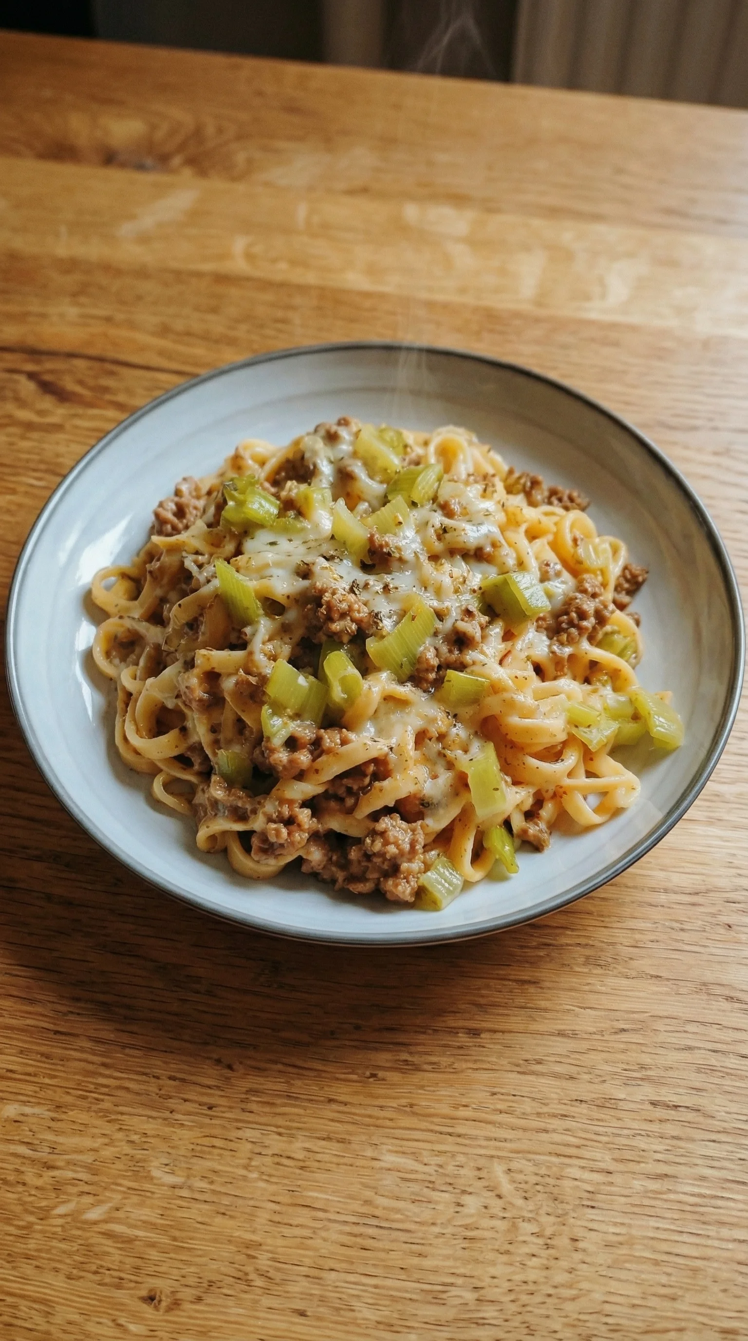Ein weißer Teller mit einer Mischung aus Pasta, Hackfleisch und Kaese.