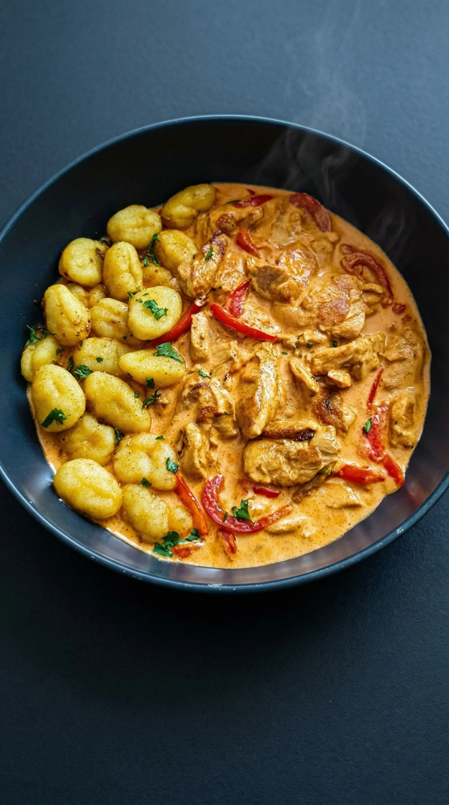 A bowl of food with chicken, gnocchi, and peppers.