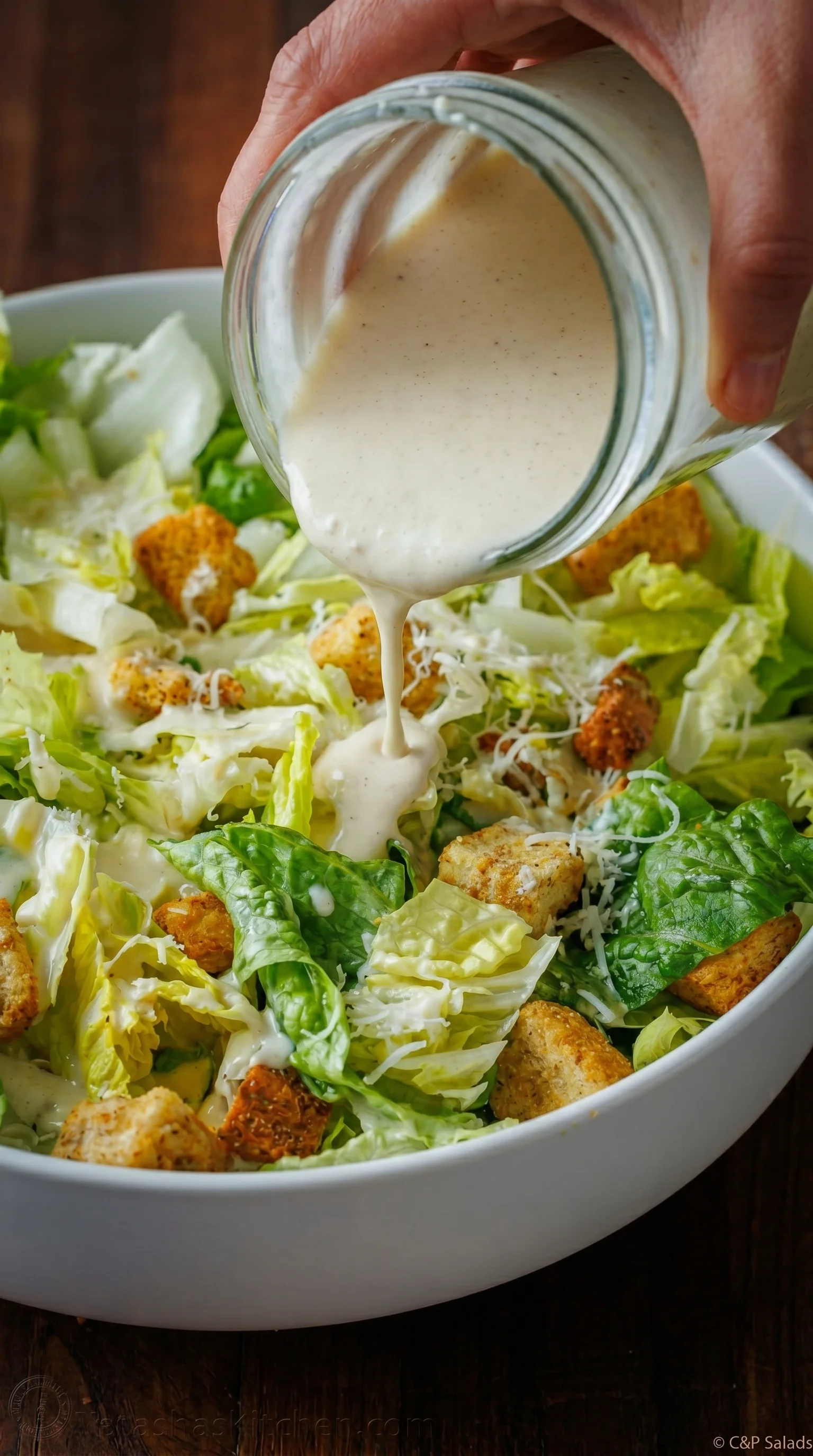 A person pouring dressing on a salad.