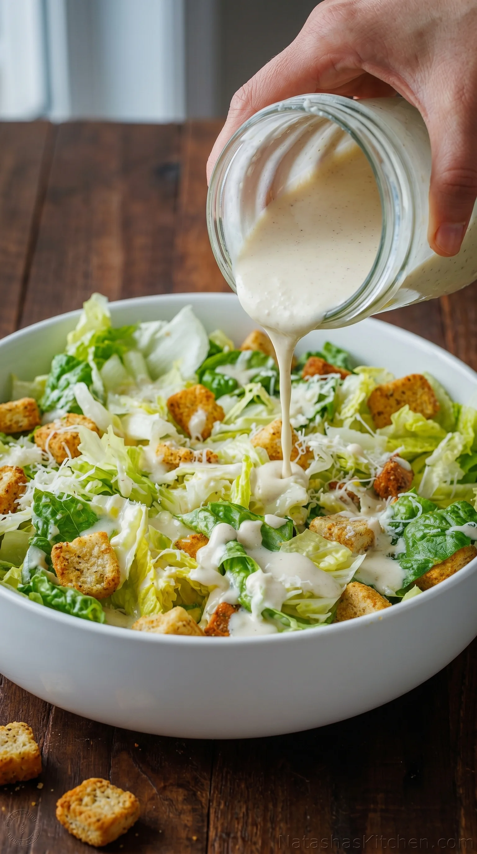 A person pouring dressing on a salad.