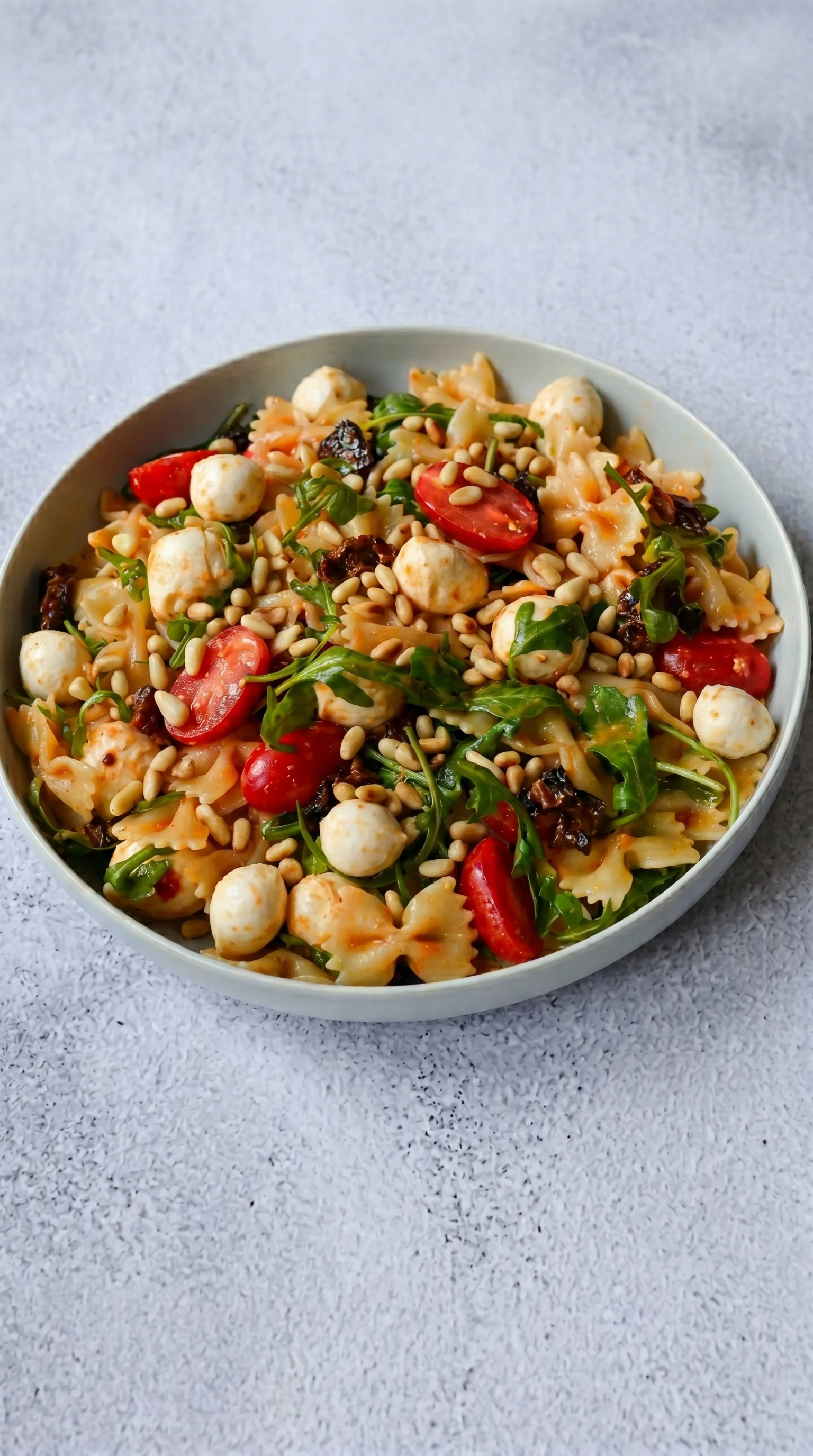 A bowl of pasta salad with tomatoes, spinach, and pine nuts.