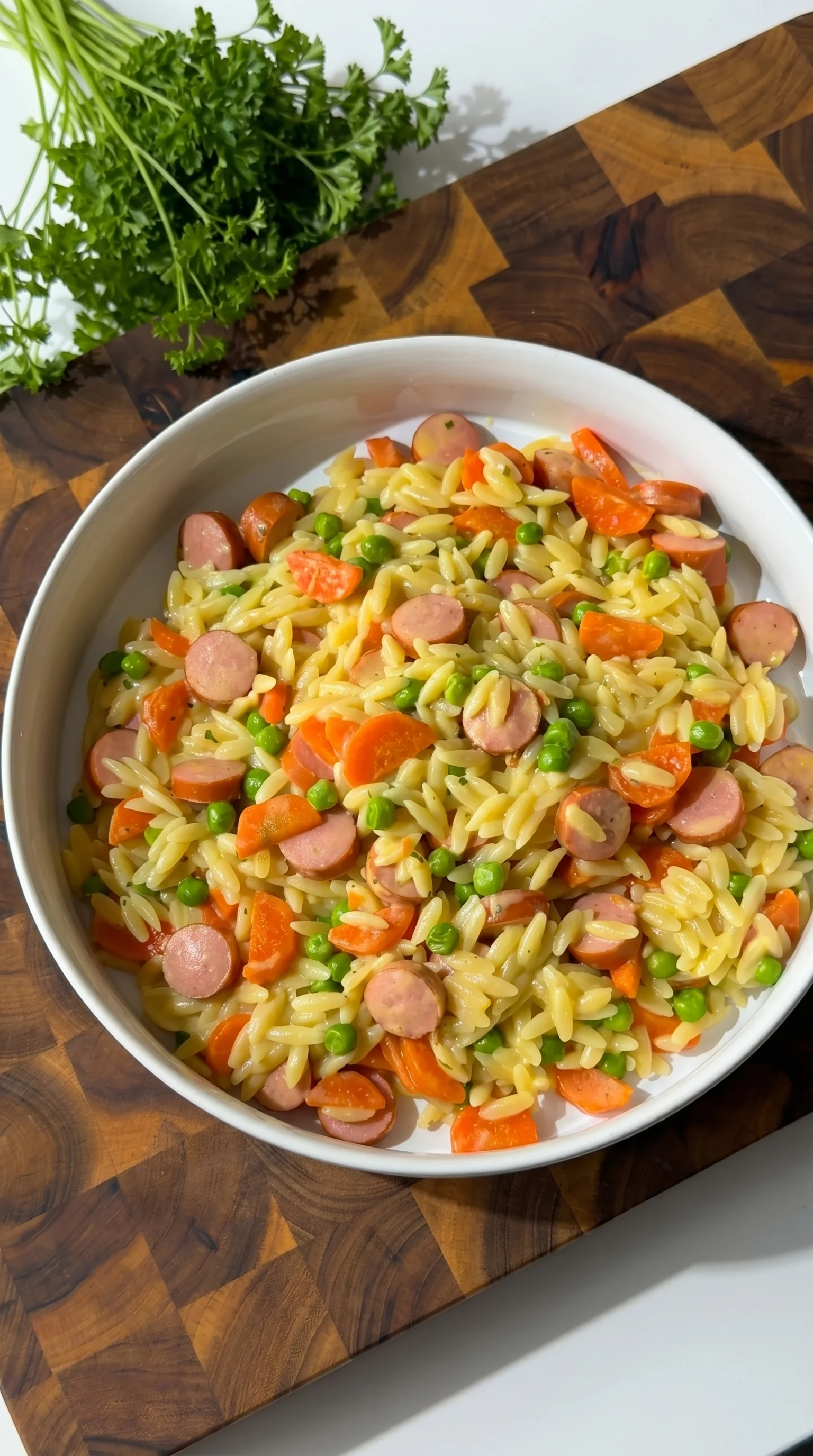 A bowl of pasta with sausage and peas.