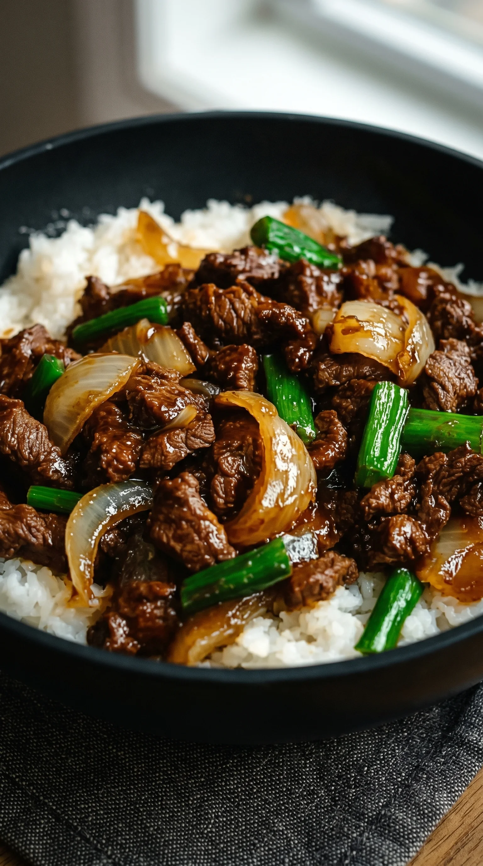 A bowl of beef with onions and rice.