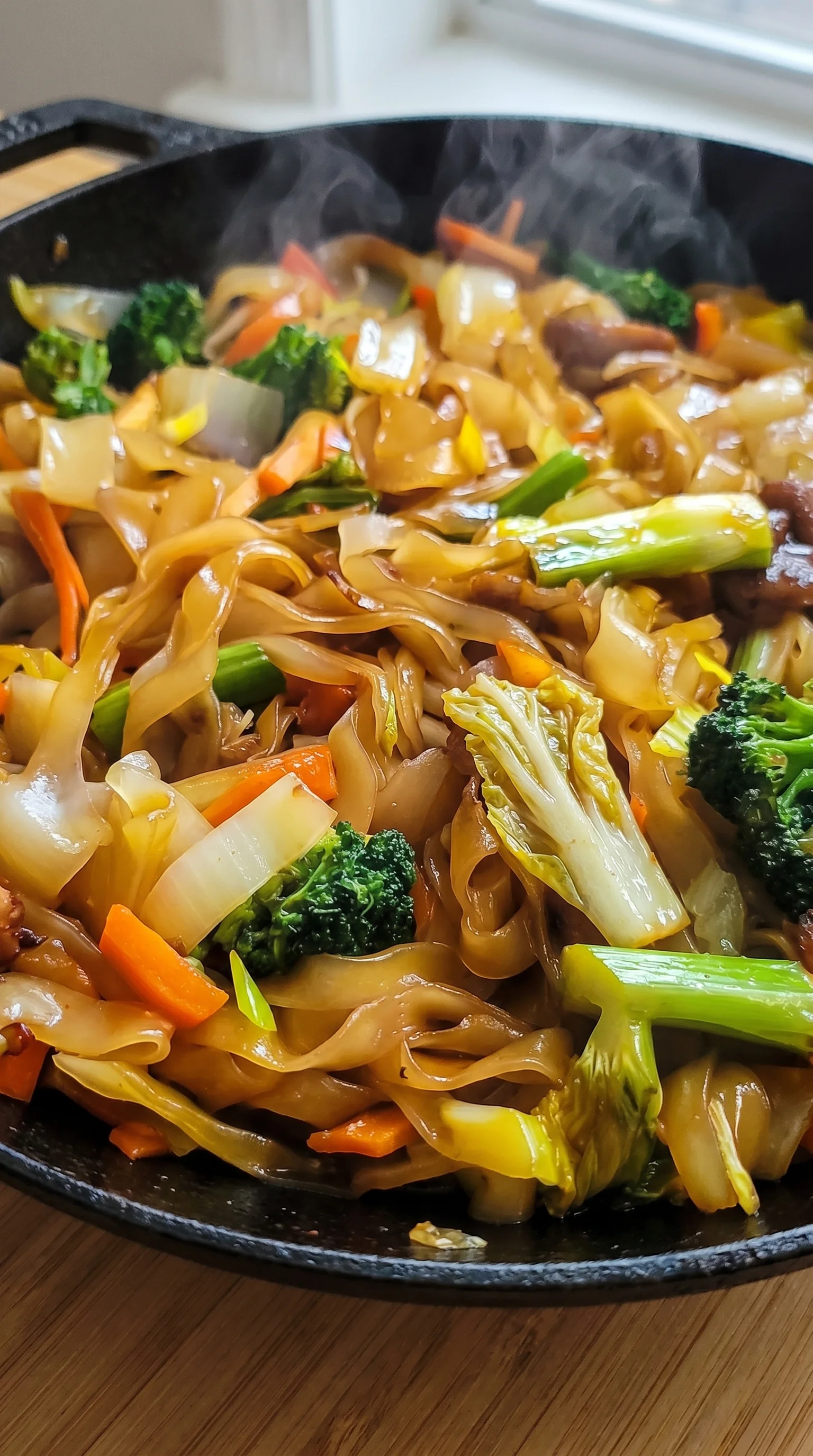 A close up of a stir fry with noodles, broccoli, carrots, and other vegetables.