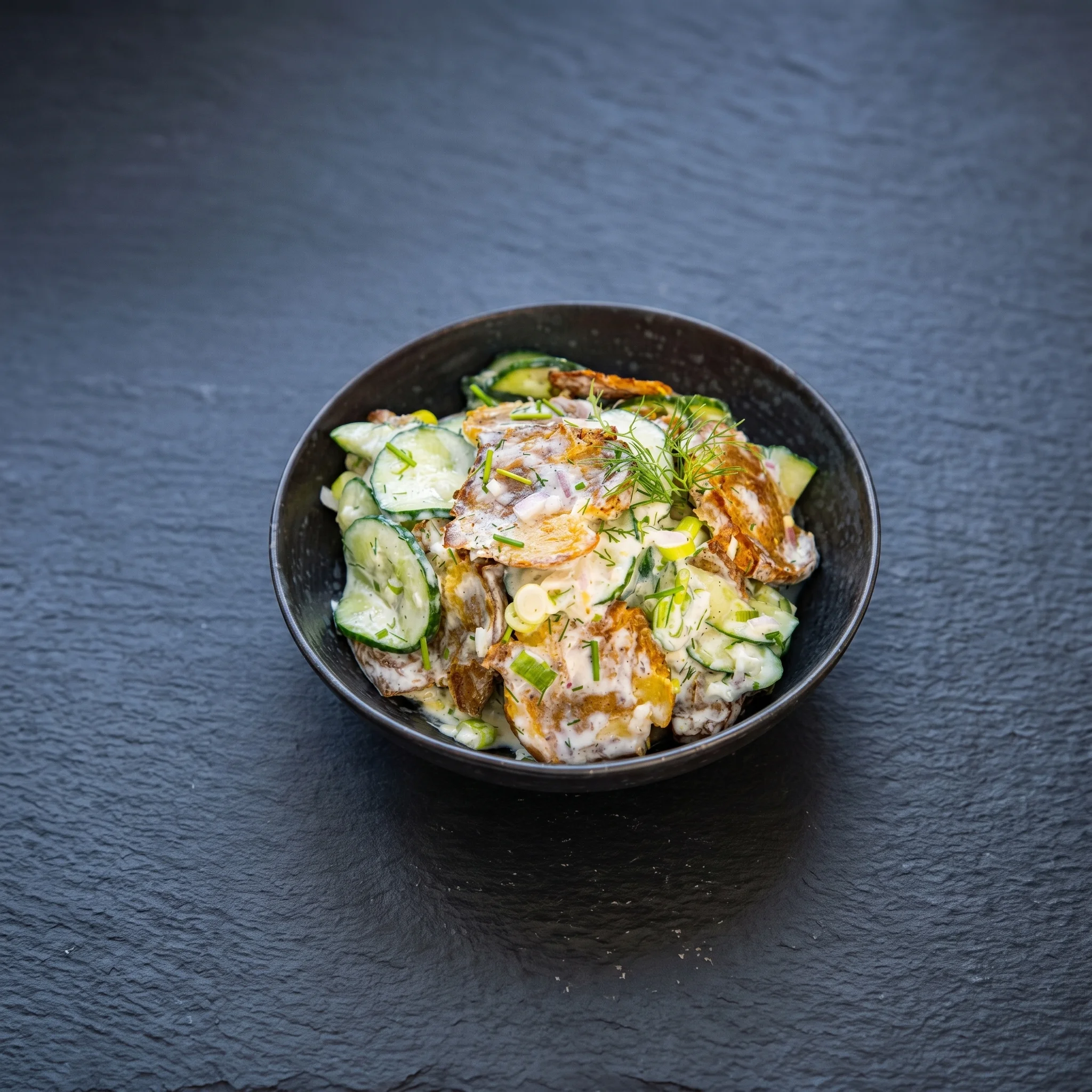 A bowl of food with cucumbers and other vegetables.