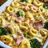 Ein weißer Teller mit einer Mischung aus Käse, Pasta, Broccoli und Ham.