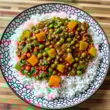 Ein Plate mit Rice und einer Mischung aus Fleisch und Gemüse, darunter Karotten, Peas und Kartoffeln.