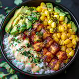 Ein schwarzes Bowl mit einer Mischung aus Reis, Kartoffeln, Avocado, Kokosnuss, Korn, Auberginen, Paprika, Zwiebeln und Tomaten.