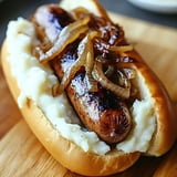 Ein Hotdog mit Kartoffeln und Zwiebeln auf einem Brett.