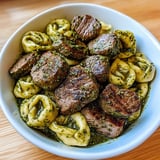 Ein weißer Teller mit einer Mischung aus Rindfleisch, Pasta und Gemüse.