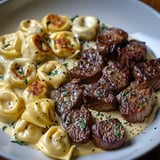 Ein weißer Teller mit einer Mischung aus Rindfleisch, Pasta und Kräutern.