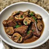 Ein weißer Teller mit einer Mischung aus Fleisch, Mushrooms und Zwiebeln.