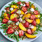 Ein weißer Teller mit einer salatartigen Beilage, die aus Strawberries, Walnuts, Pecans, Peaches, Gorgonzola und Spinach besteht.