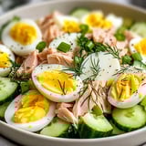 Ein weißer Teller mit Eiern, Salat und Fisch.